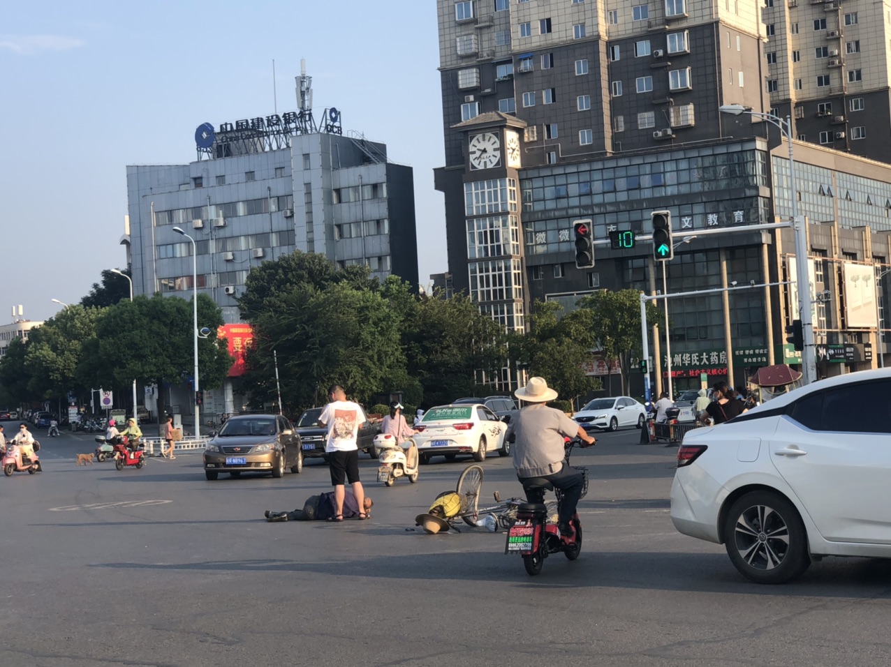 翠微西路十字路口一辆白色轿车撞倒骑自行车的老人,老人侧躺在地头上